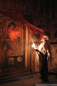 Ethiopian priest showing the church frescoes by candlelight